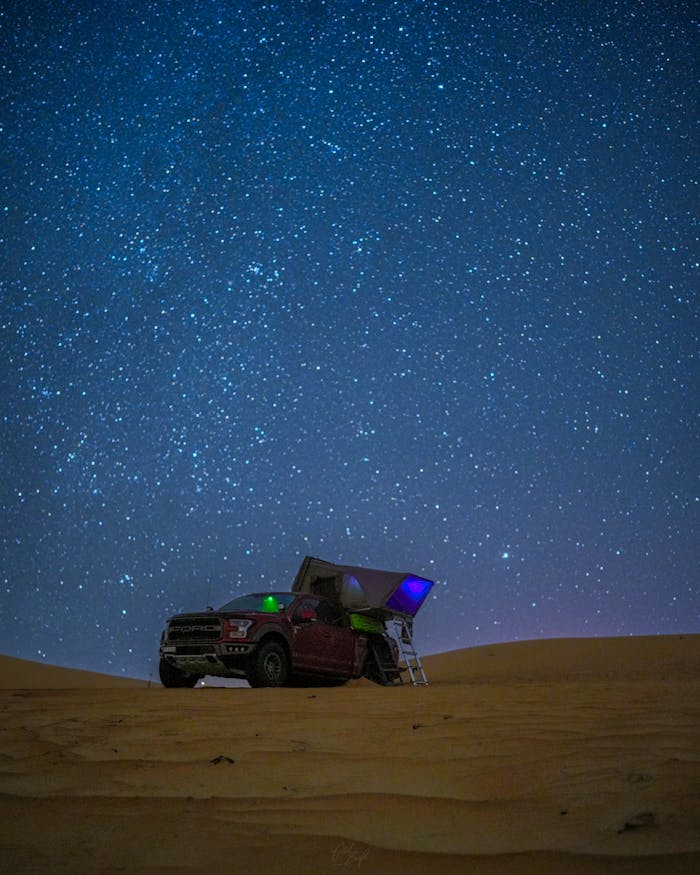 Off-road vehicle with rooftop tent under a starry desert sky, ideal for exploring night landscapes.